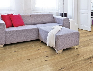 Im Wohnzimmer ist Parkett in Langdielen-Optik verlegt. Dazu passt ein Ecksofa mit bunten Kissen.