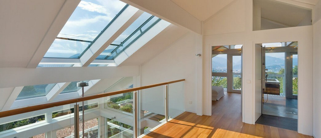 Modernes Dachgeschoss mit großen Glasdachfenstern, Holzfußboden und Glasgeländer, lichtdurchflutet mit Panoramablick.