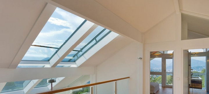 Modernes Dachgeschoss mit großen Glasdachfenstern, Holzfußboden und Glasgeländer, lichtdurchflutet mit Panoramablick.