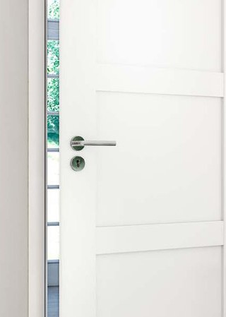 Weiße Innentür mit Edelstahlgriff, teilweise geöffnet, mit Blick auf Garten im Hintergrund.