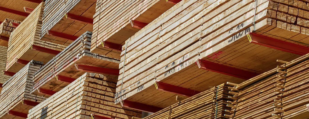 Gestapeltes Bauholz in einem Lagerregal mit roten Trägern, bereit für den Holzbau und die Weiterverarbeitung.